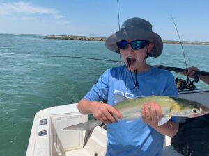 Boy with excited expression holds a freshly caught fish while fishing in Murrells Inlet in August 2026.