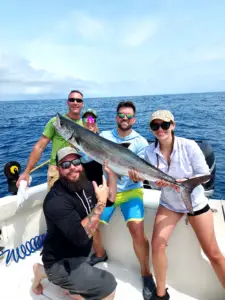 Five smiling people on a boat holding a large king mackerel