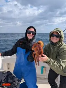 Two women on a boat in Murrells Inlet, South Carolina, holding an octopus during winter fishing.