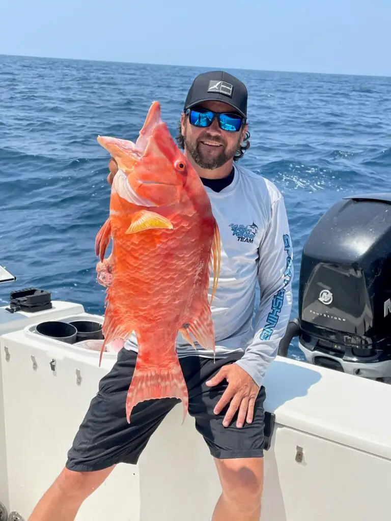 Man in fishing shirt holding a large red snapper on a boat