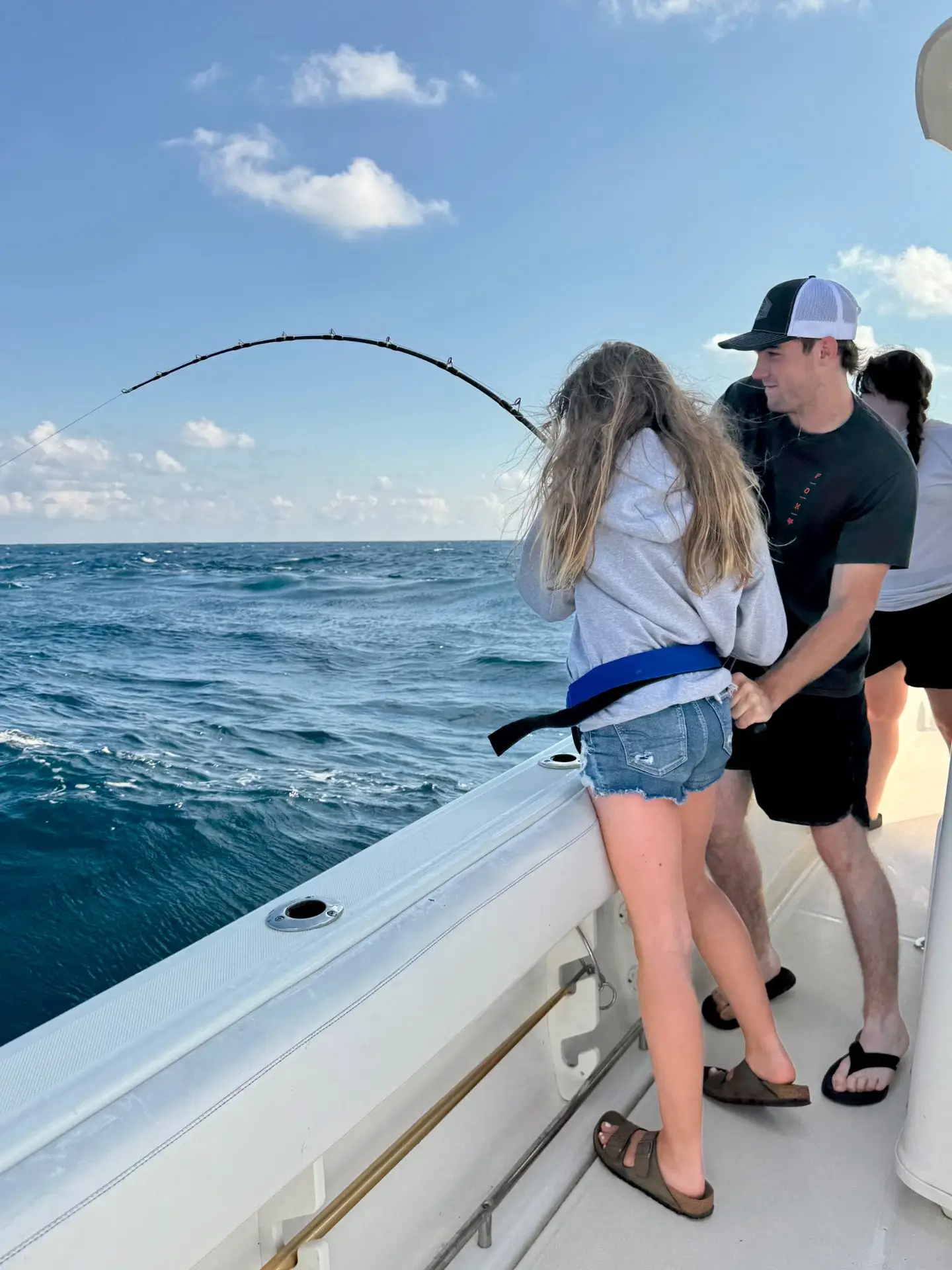 Teens fishing on a boat, with a rod bent from a catch