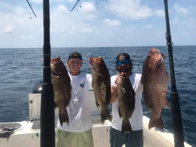 Two men on a boat proudly display their large fish catch in the ocean.