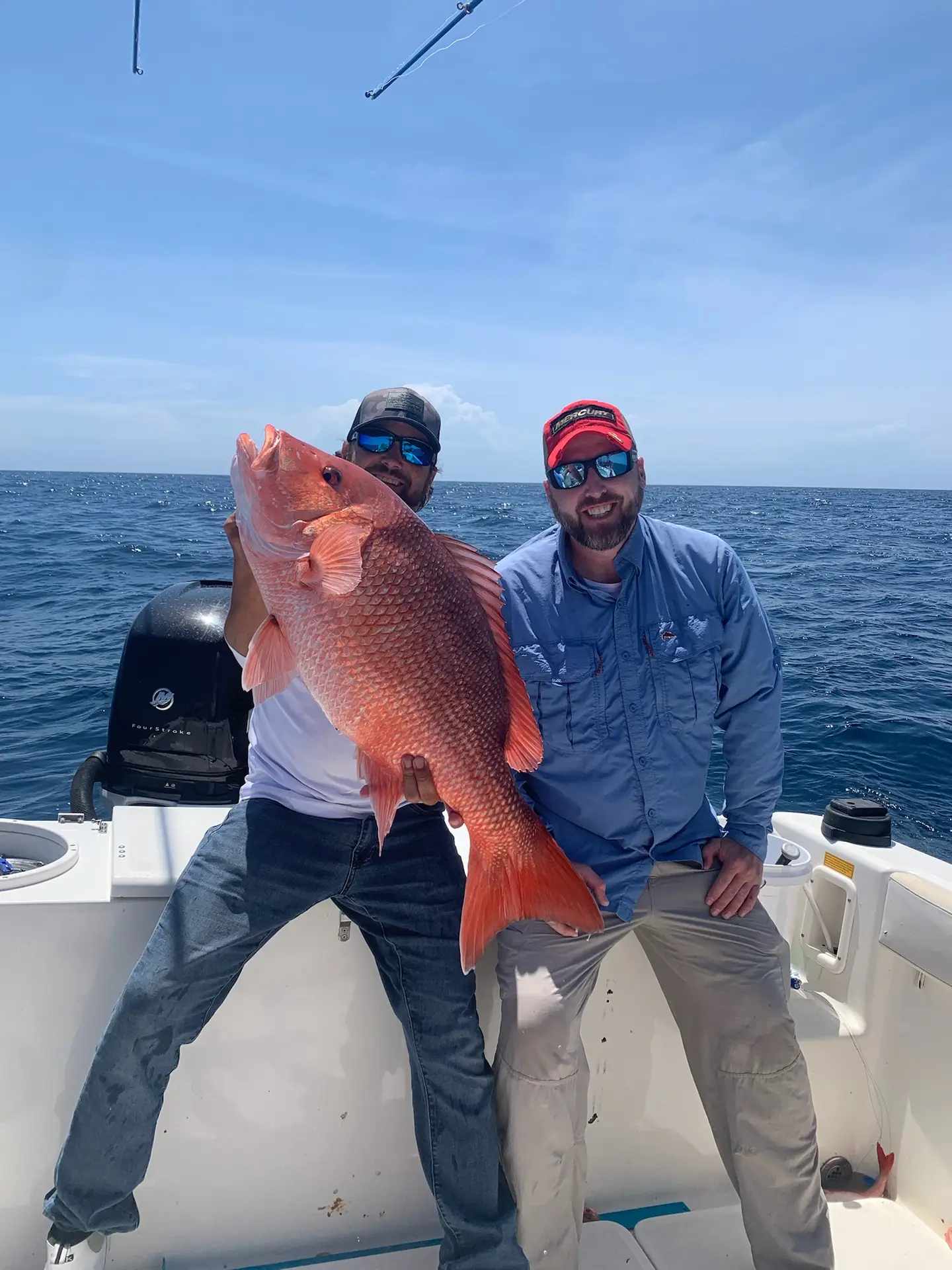 Two men on a boat proudly display a large red snapper caught while fishing.