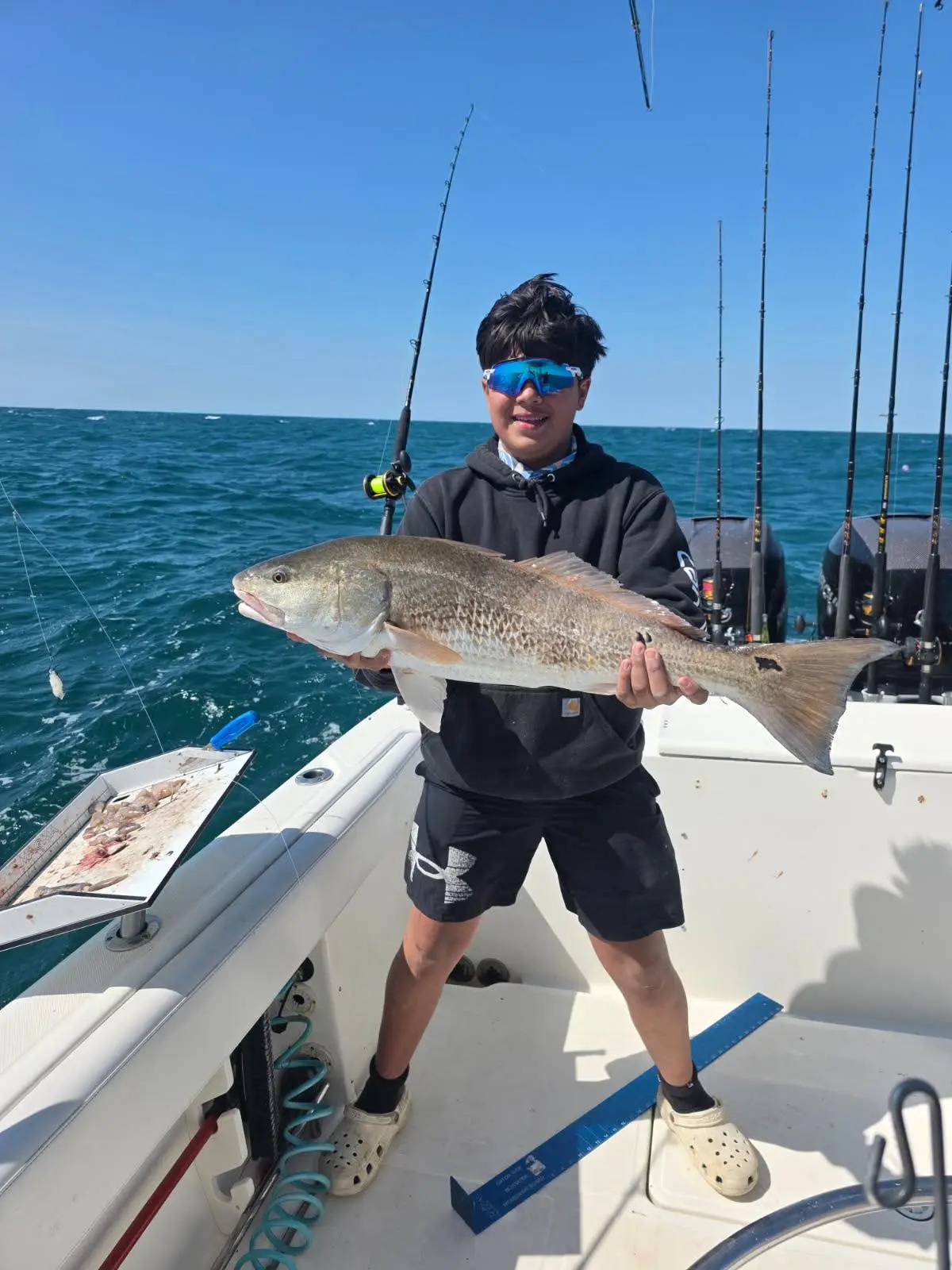 Young angler proudly displays a large red drum fish on a boat.