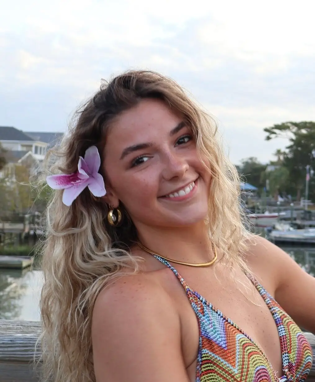 Young woman with a flower in her hair smiles at the camera in a colorful bikini.