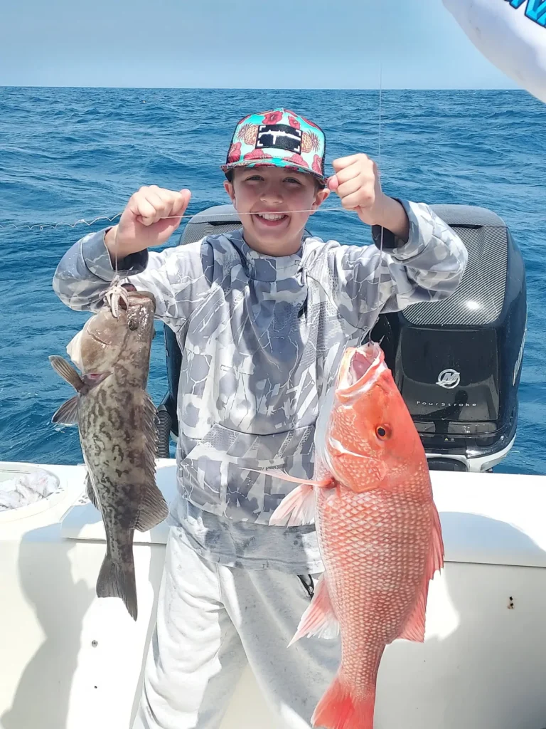 Boy holding two fish on a fishing charter, showing off his catch.