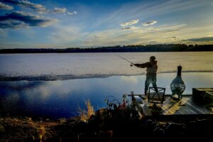 Man fishing on a dock in late autumn with ice forming on the lake